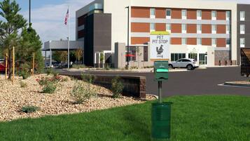 Un edificio con un letrero para zona de parada de mascotas, un estacionamiento y un área verde con árboles.