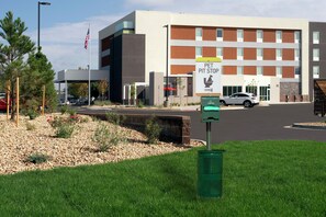 A building with a sign for a pet pit stop, a parking lot, and a grassy area with trees. - Home2 Suites by Hilton Longmont (Longmont)