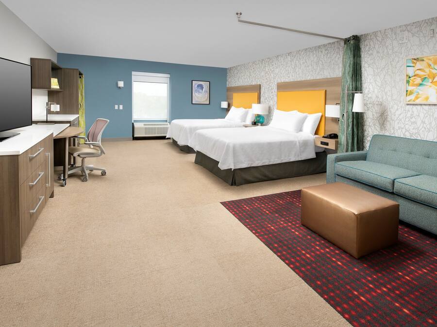 A hotel room with a desk, two beds, a sofa, a television, and a large window.