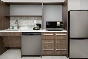 A modern kitchen with a built-in dishwasher, a stainless steel refrigerator, and a microwave on the countertop. - Home2 Suites by Hilton Longmont (Longmont)