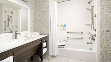 A modern bathroom with a large mirror, dual sinks, a vanity, a shower with grab bars, and a bathtub.