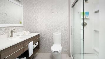 A modern bathroom with a white toilet, a glass-enclosed shower, and a sink with a mirror above it.