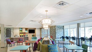 A modern cafe with a central seating area, a coffee bar, and large windows offering a view of the outdoors. - Home2 Suites by Hilton Richmond Hilll Savannah I-95 (Richmond Hill)