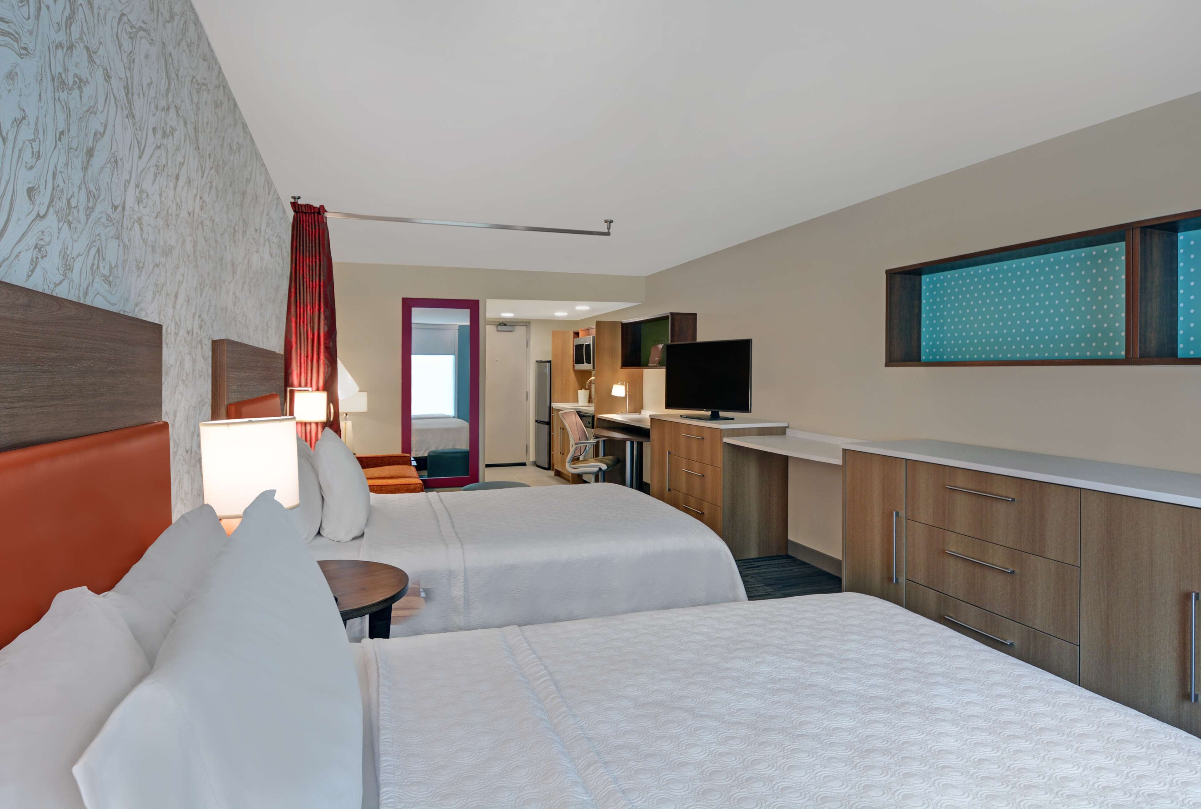 A hotel room with two beds, a desk, a TV, and a bathroom visible through an open door.