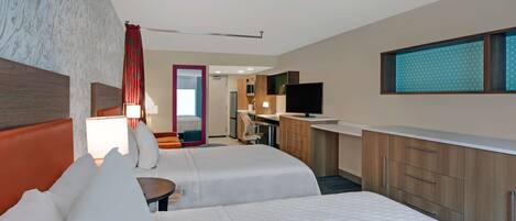 A hotel room with two beds, a desk, a TV, and a bathroom visible through an open door.