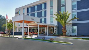 A modern hotel with a covered outdoor seating area, a stone facade, and a flag. - Home2 Suites by Hilton Richmond Hilll Savannah I-95 (Richmond Hill)