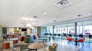 A spacious indoor area with multiple seating arrangements, including sofas and chairs, and a counter with a display. - Home2 Suites by Hilton Richmond Hilll Savannah I-95 (Richmond Hill)