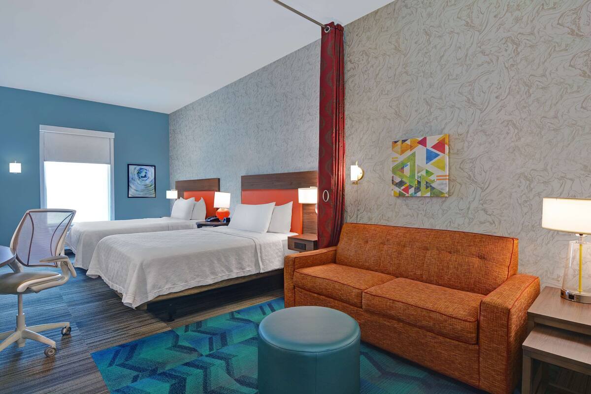A hotel room with two beds, a sofa, a desk, and a chair.