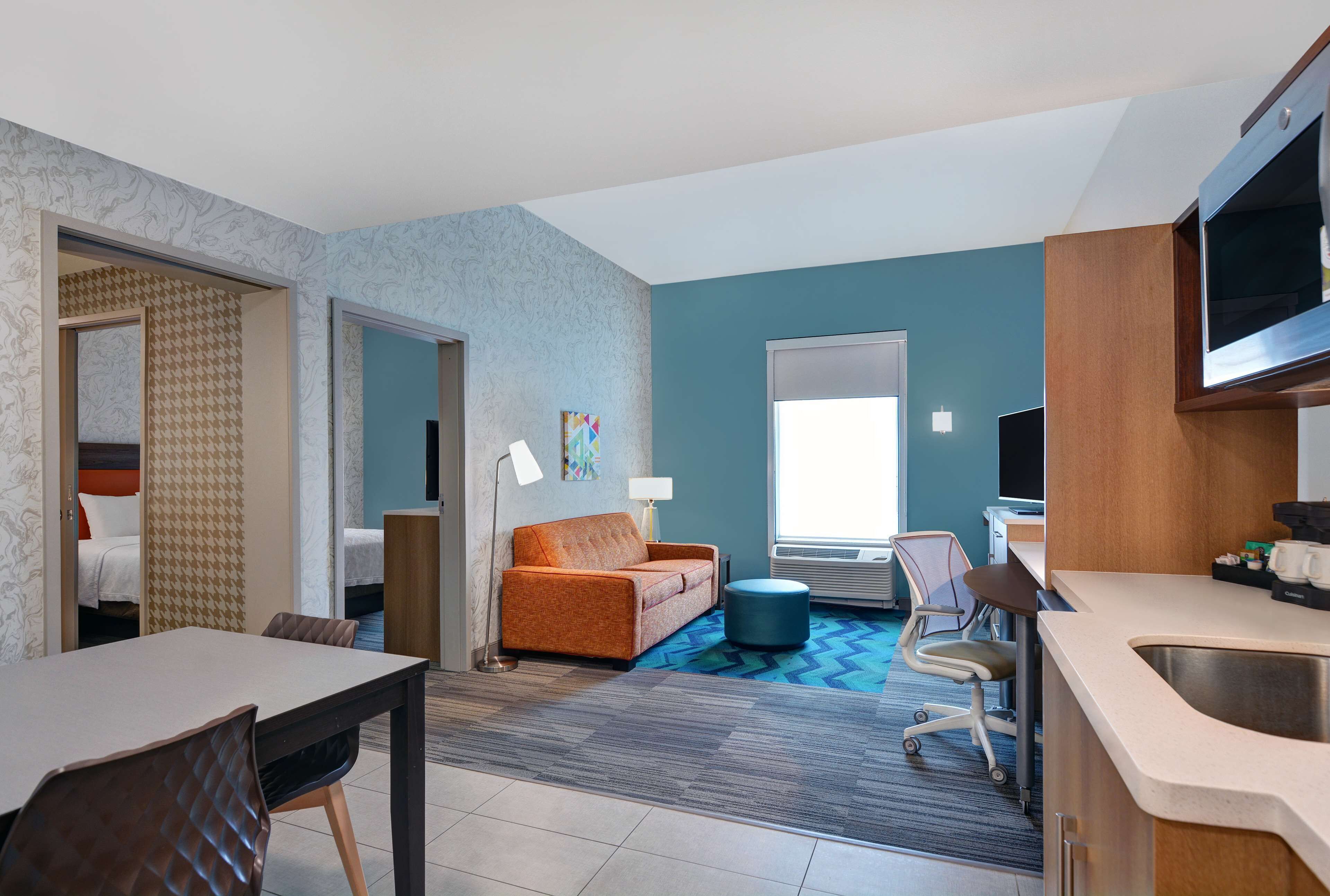 A hotel room with a dining area, a sofa, a TV, and a kitchenette.