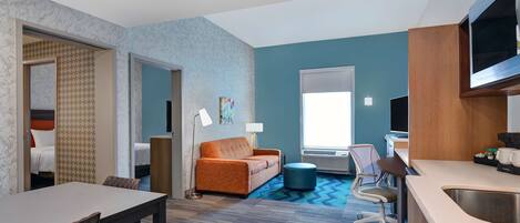 A hotel room with a dining area, a sofa, a TV, and a kitchenette.