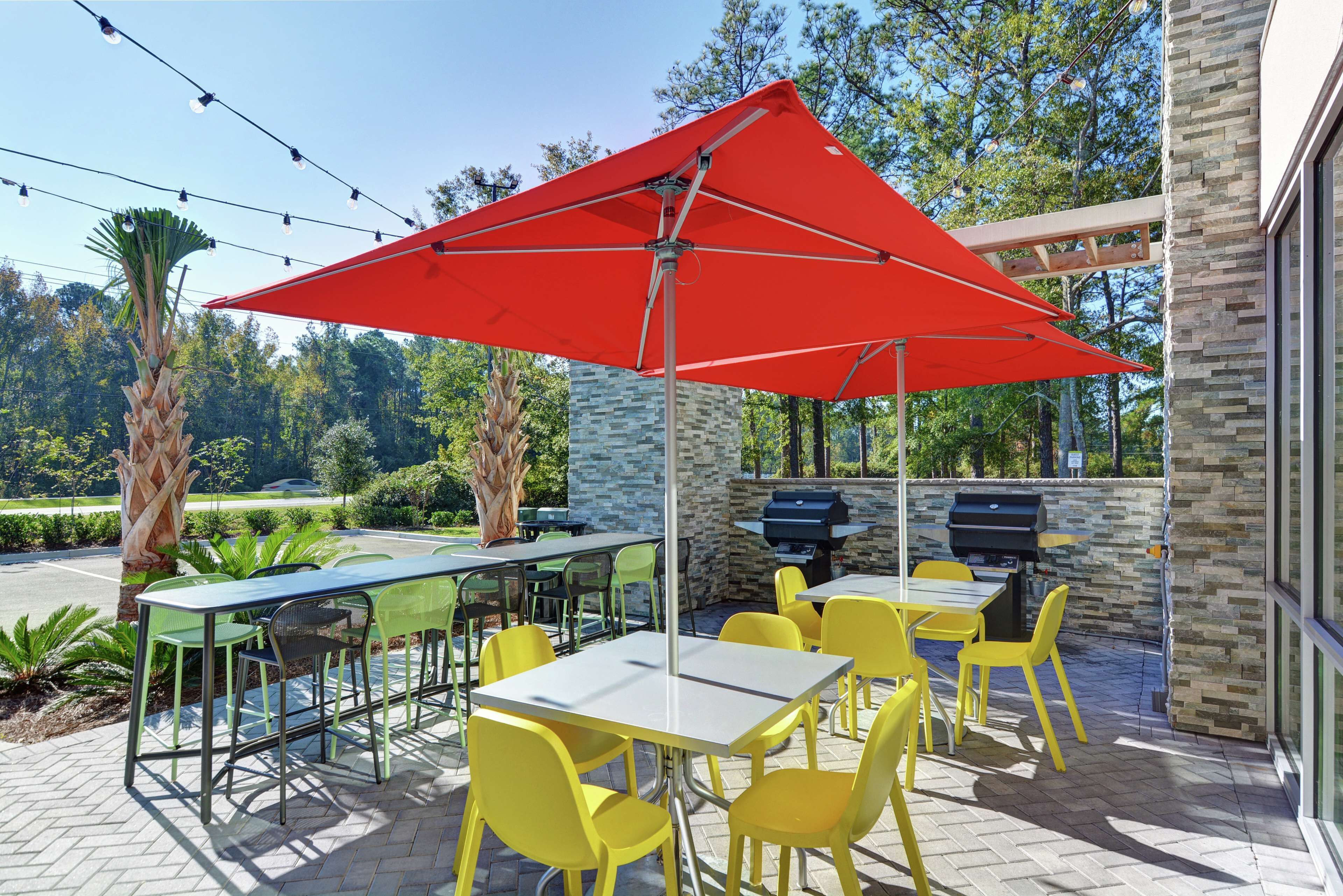 An outdoor patio with tables and chairs, a red umbrella, and a stone wall.