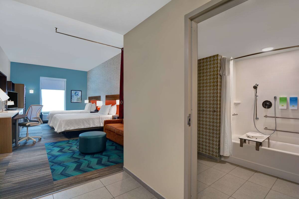 A hotel room with a bed, a desk, a chair, a small table, and a bathroom with a bathtub and shower.