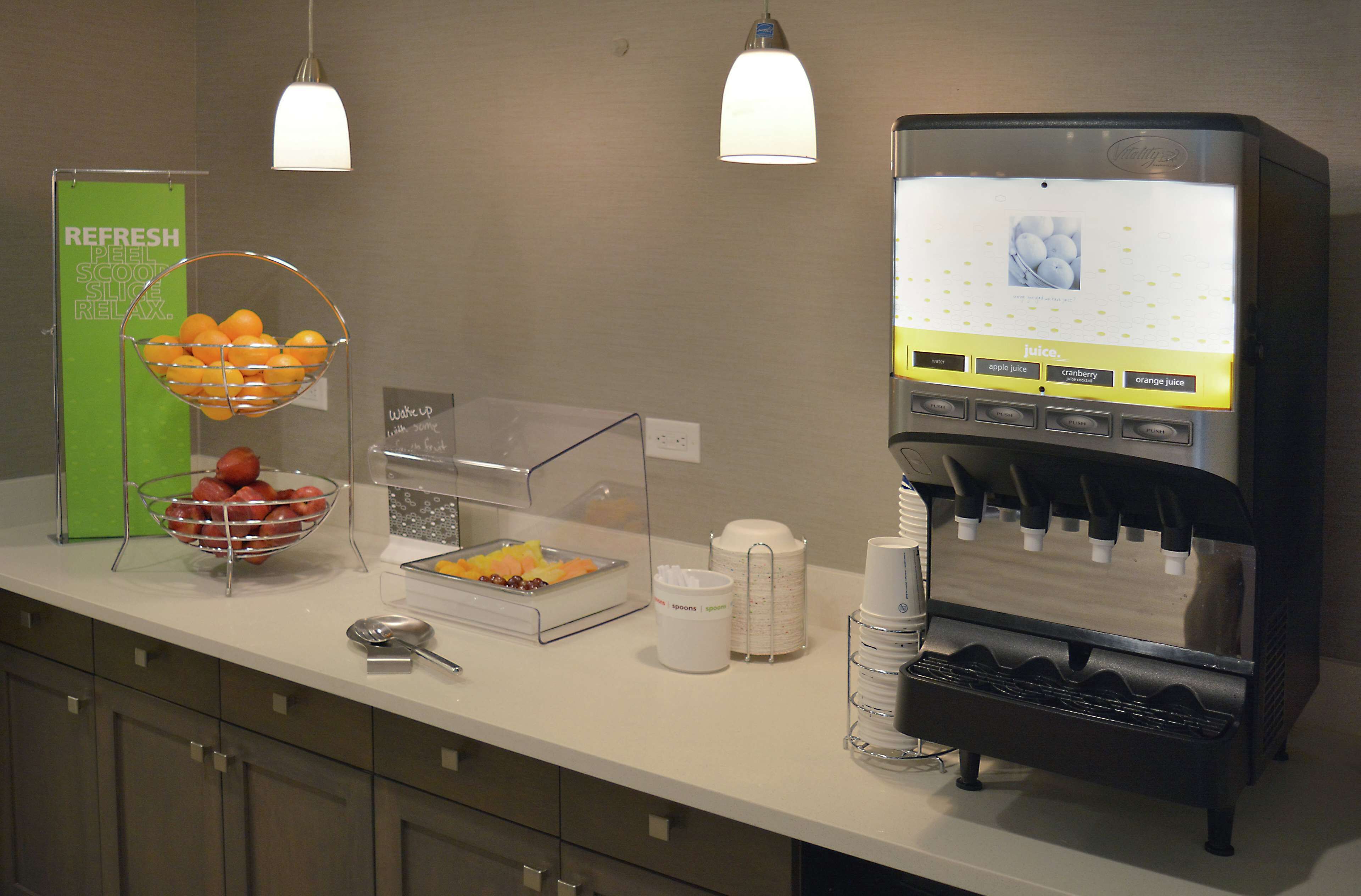 A self-serve beverage station with a selection of juices and a fruit bowl.