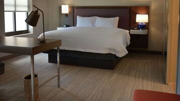 A hotel room with a bed, bedside table, lamp, and a small trash bin.
