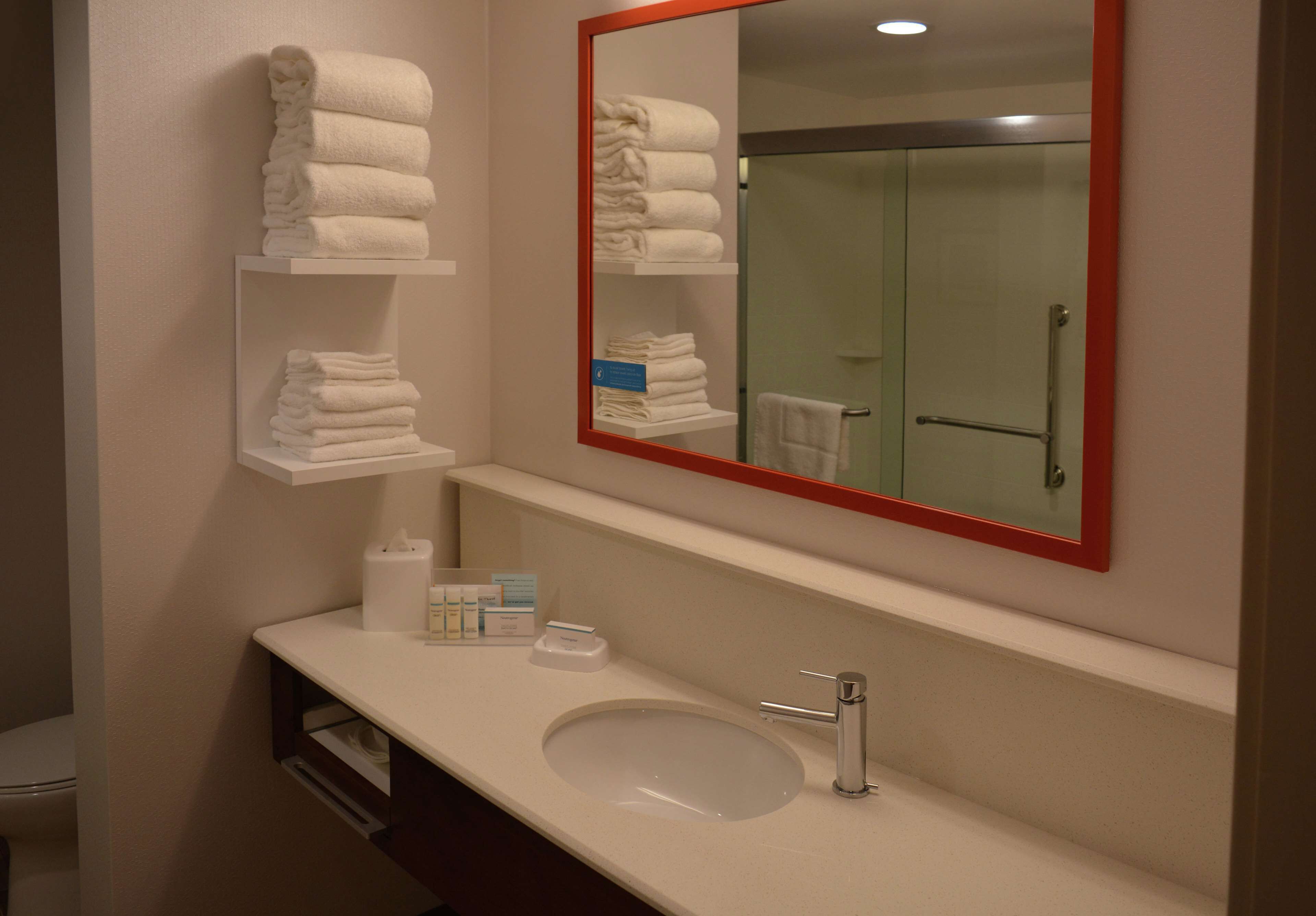 Un baño con lavamanos, espejo y repisas con toallas.