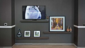 En väggmonterad TV som visar en webbplats, inramade bilder och dekorativa vaser på hyllor.