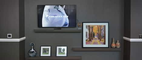 A wall-mounted TV displaying a website, framed pictures, and decorative vases on shelves.