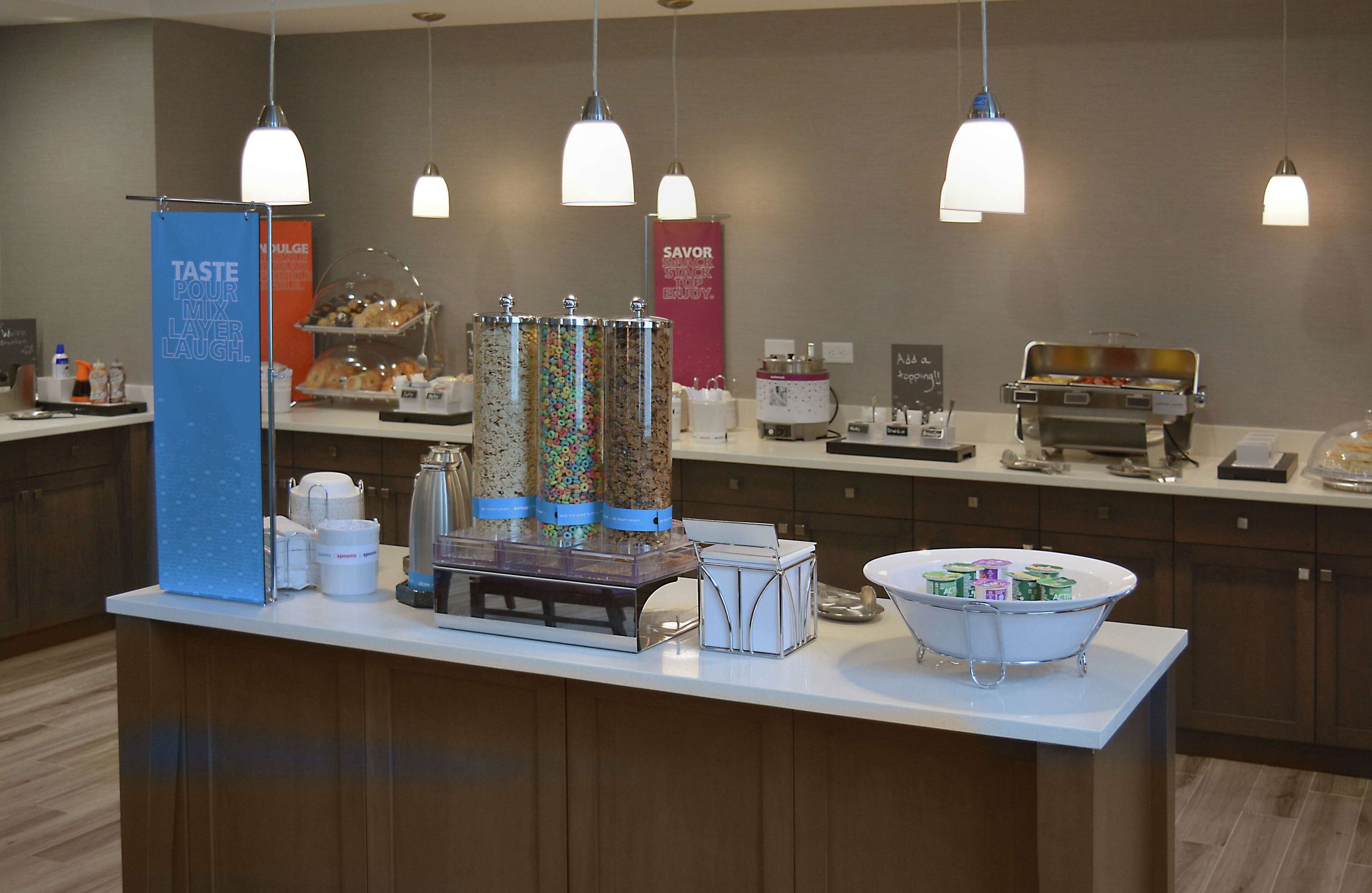 Una barra de desayuno con varios recipientes de comida, una máquina de café y un fabricante de gofres.