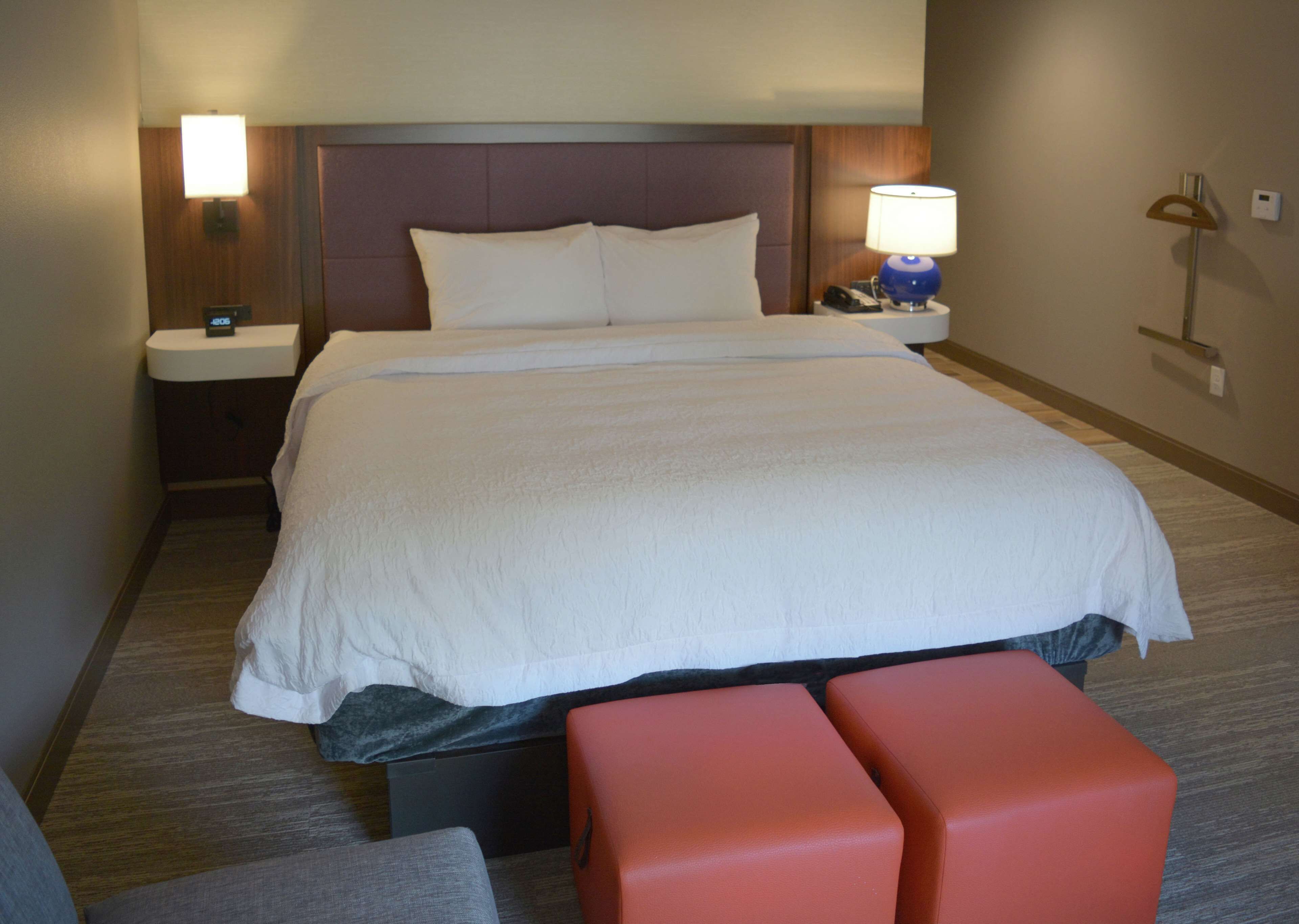 A hotel room with a large bed, a bedside table with a lamp, a small desk, and a bench.