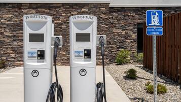 Duas estações de carregamento para veículos elétricos com a identificação 'EV INSTITUTE', e uma placa próxima indicando 'CARREGAMENTO DE VEÍCULOS ELÉTRICOS'.