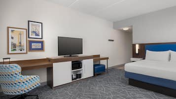 Una habitación de hotel con cama, un escritorio con televisor, una silla y dos cuadros en la pared.