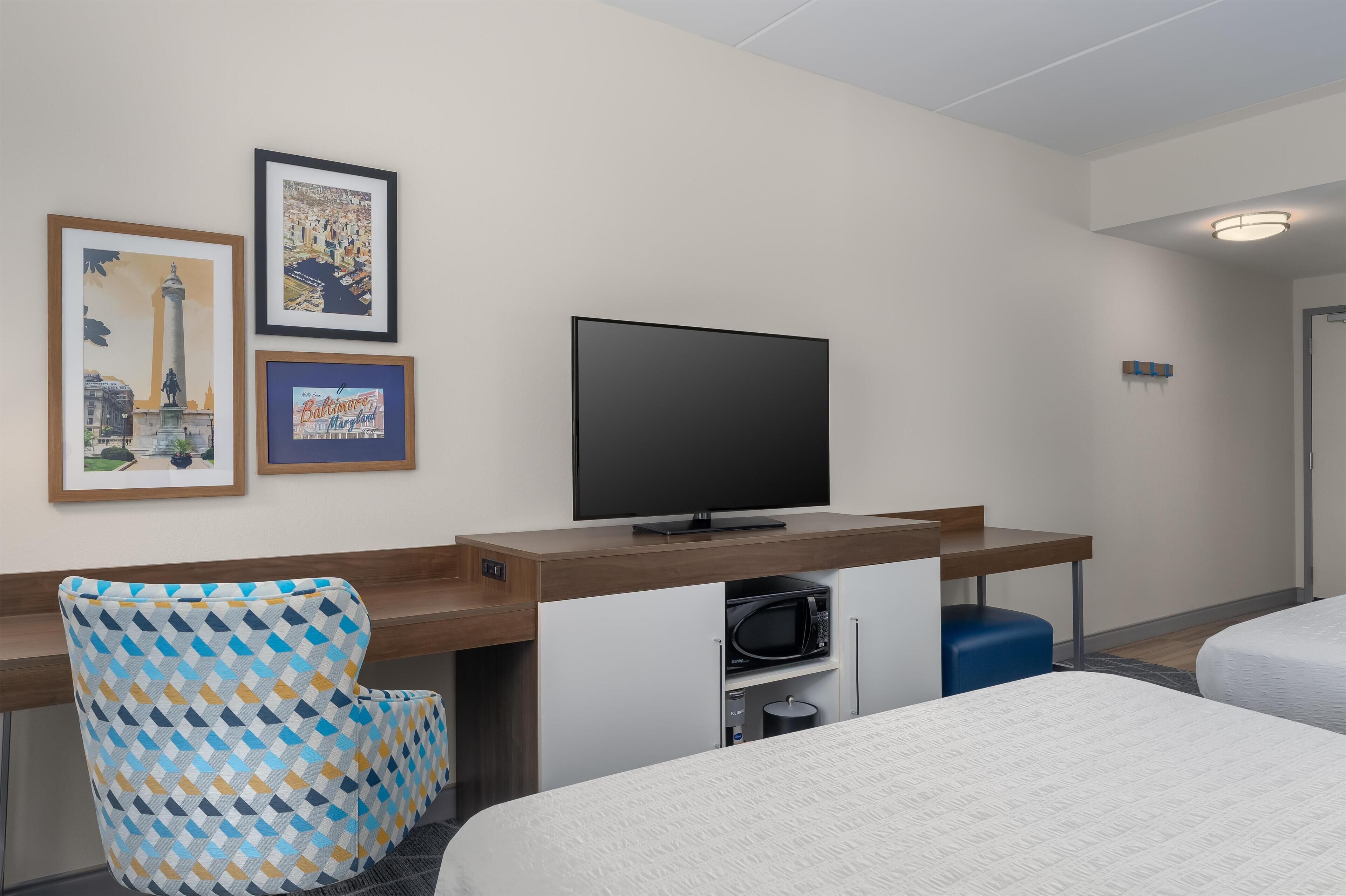 Una camera d'albergo con un letto, una scrivania con televisore, una sedia e due quadri appesi al muro.