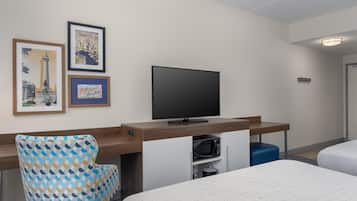 Una camera d'albergo con un letto, una scrivania con televisore, una sedia e due quadri appesi al muro.