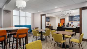 Un comedor de hotel con varias mesas y sillas, una zona de bar y vistas a la ciudad.