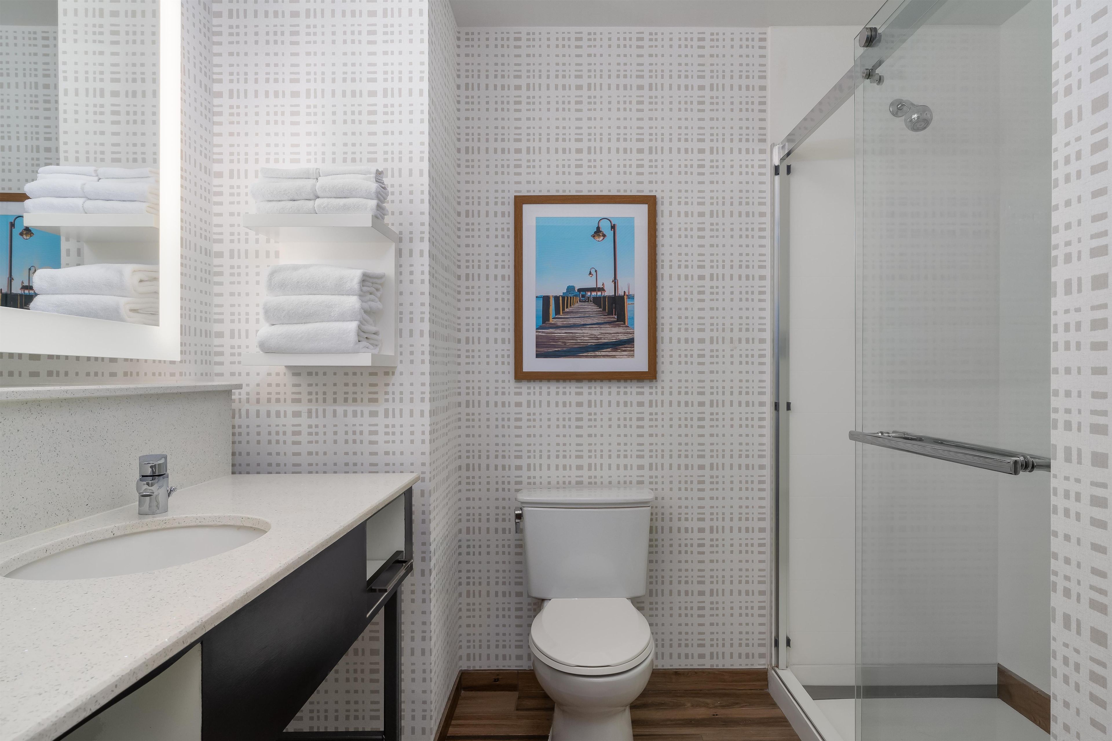 A modern bathroom with a white sink, a toilet, and a shower. There is a framed picture on the wall.