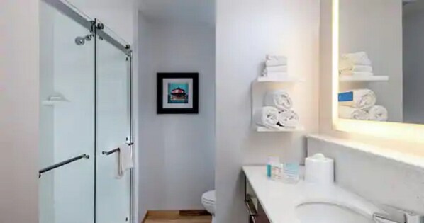 A modern bathroom with a glass shower enclosure, a toilet, a sink with a mirror, and a framed picture on the wall.