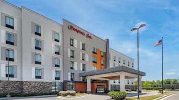 Un hotel Hampton Inn con fachada moderna, una entrada acogedora y una bandera estadounidense.