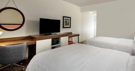 A hotel room with two beds, a desk with a television, a chair, and a microwave.