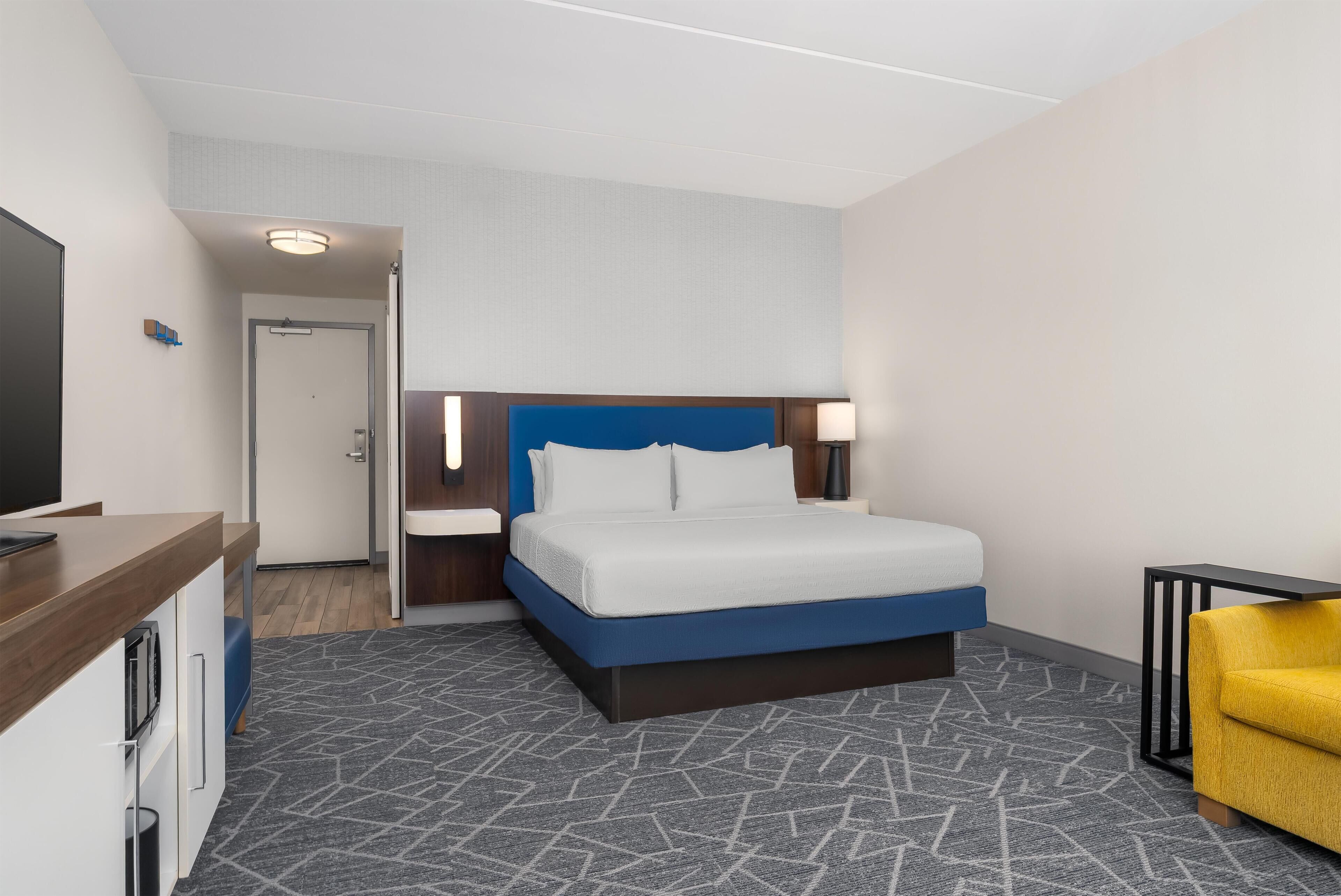A hotel room with a bed, bedside table, lamp, and a TV.