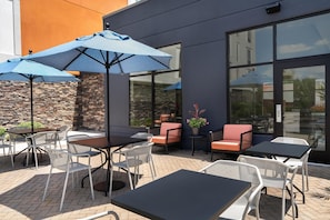 An outdoor seating area with tables and chairs, umbrellas, and a stone wall. - Hampton Inn Baltimore Bayview Campus (Baltimore)