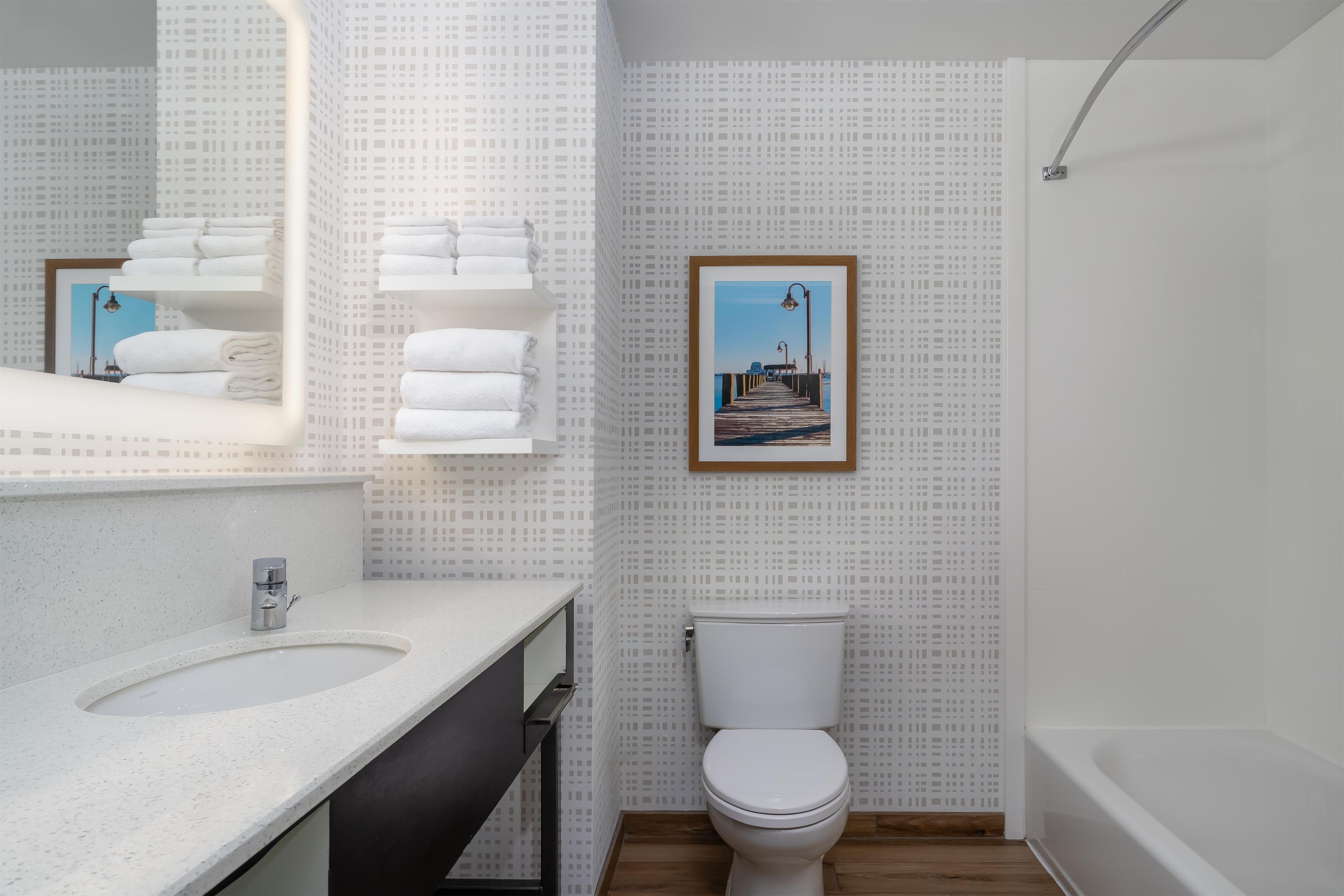 A modern bathroom with a sink, toilet, and bathtub. There is a framed picture on the wall.