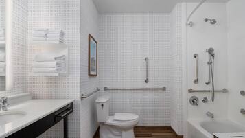 A bathroom with a toilet, a sink, a shower with grab bars, and a towel rack.