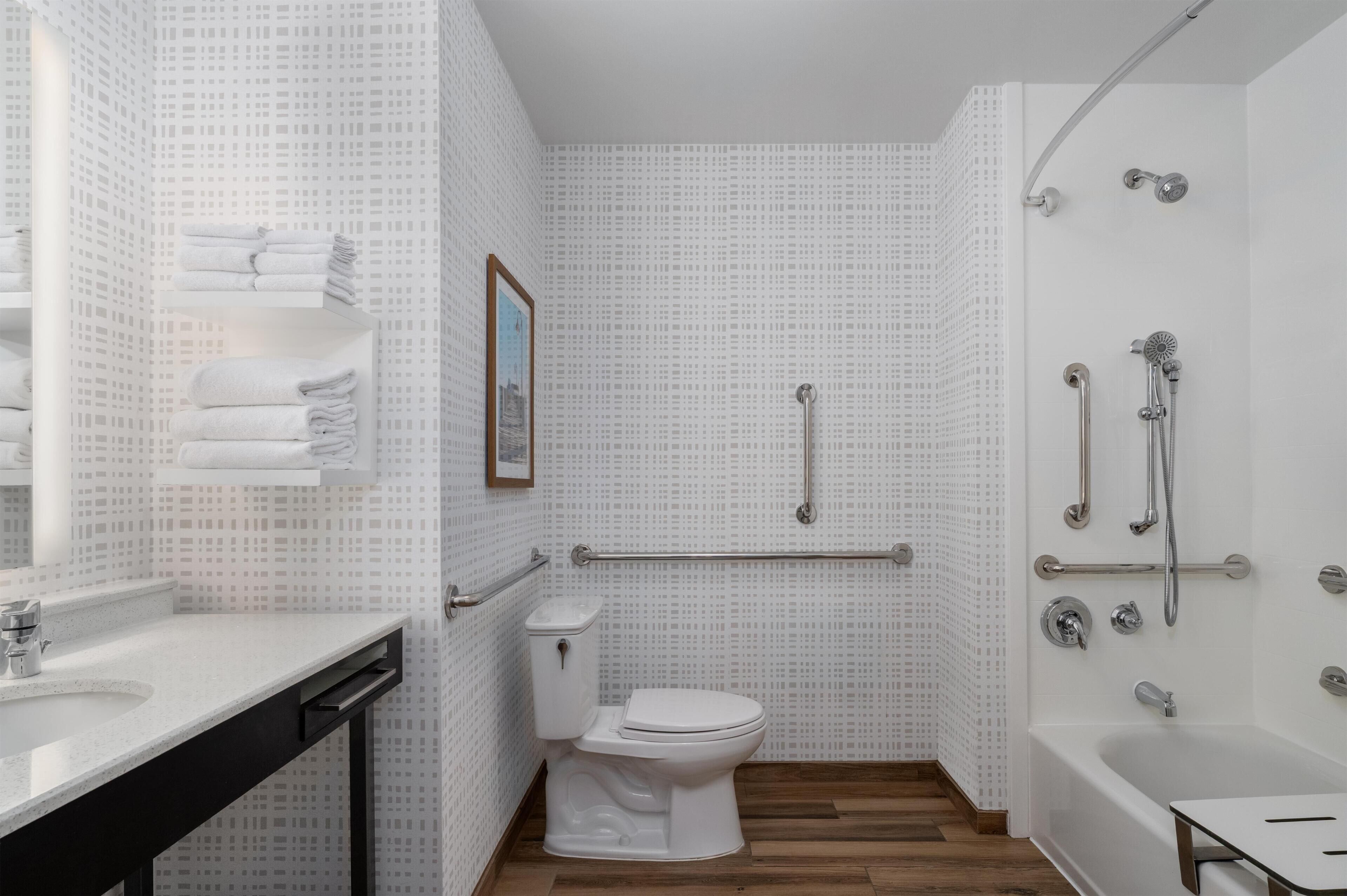 Een badkamer met toilet, wastafel, douche met handgrepen en een handdoekrek.