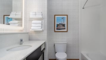 A modern bathroom with a sink, toilet, and bathtub. There is a framed picture on the wall.