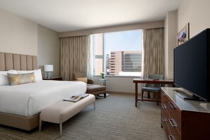 A hotel room with a large bed, a desk, a television, and a view of the cityscape.