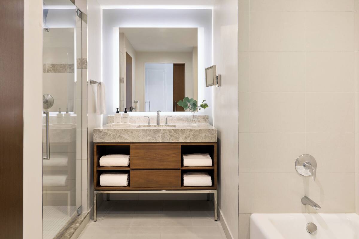 A modern bathroom with a glass shower enclosure, a marble sink, and a wooden vanity with built-in shelves.