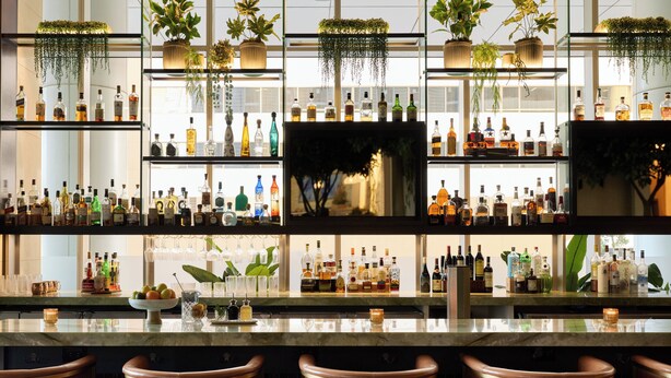 A bar area with multiple shelves of liquor bottles, hanging plants, and bar stools. - InterContinental Houston by IHG (Houston)