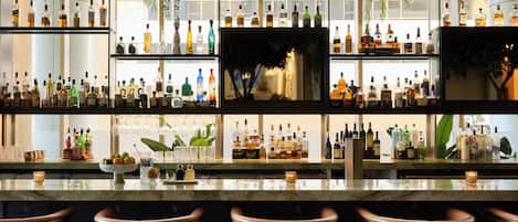 A bar area with multiple shelves of liquor bottles, hanging plants, and bar stools.