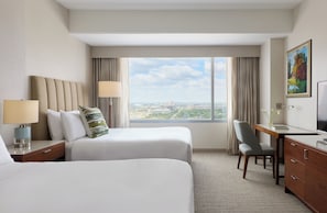 Une chambre d’hôtel avec deux lits, un bureau, une chaise, une télévision et une grande fenêtre donnant sur la ville.
