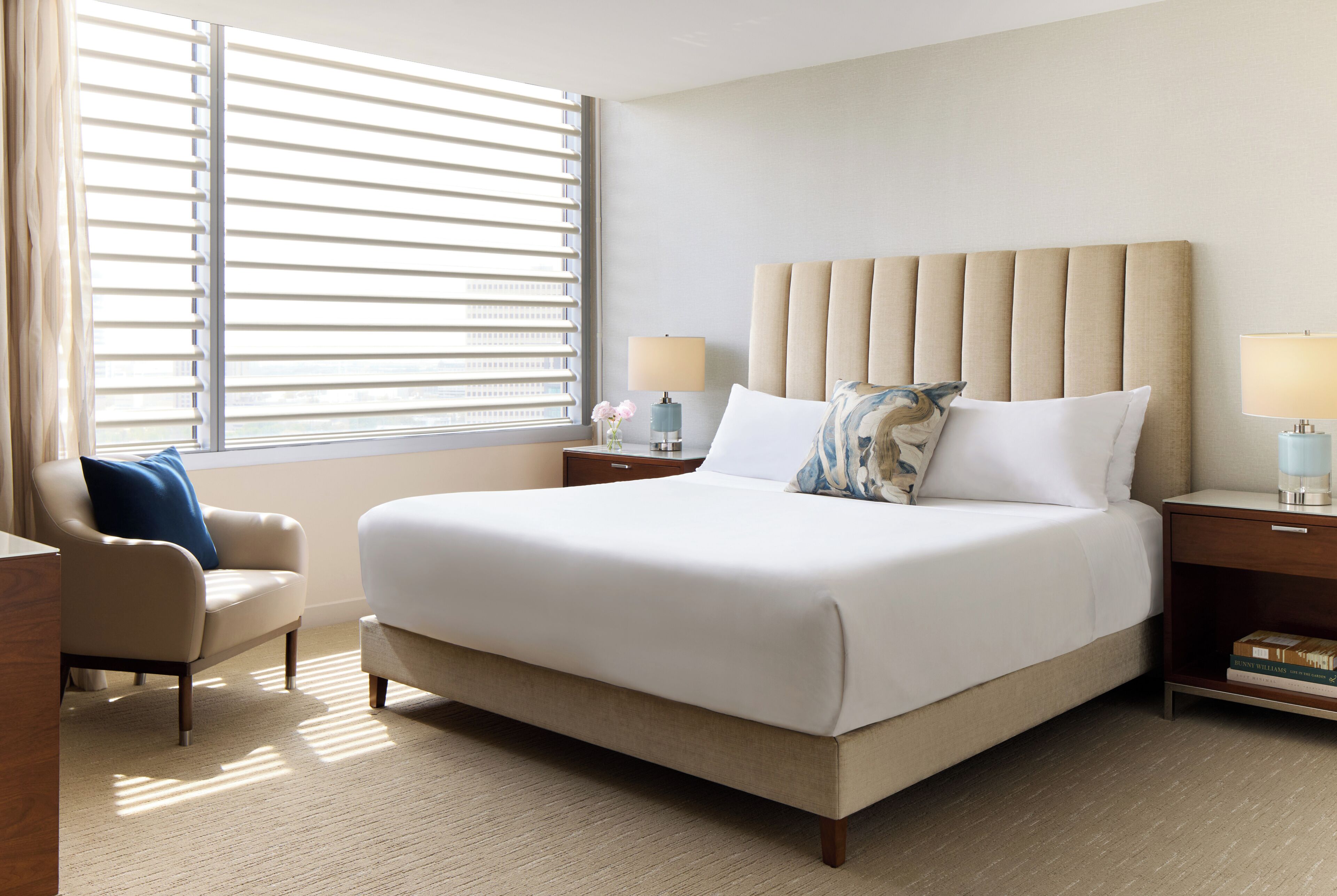 A hotel room with a large bed, a chair, a nightstand, and a window with blinds.