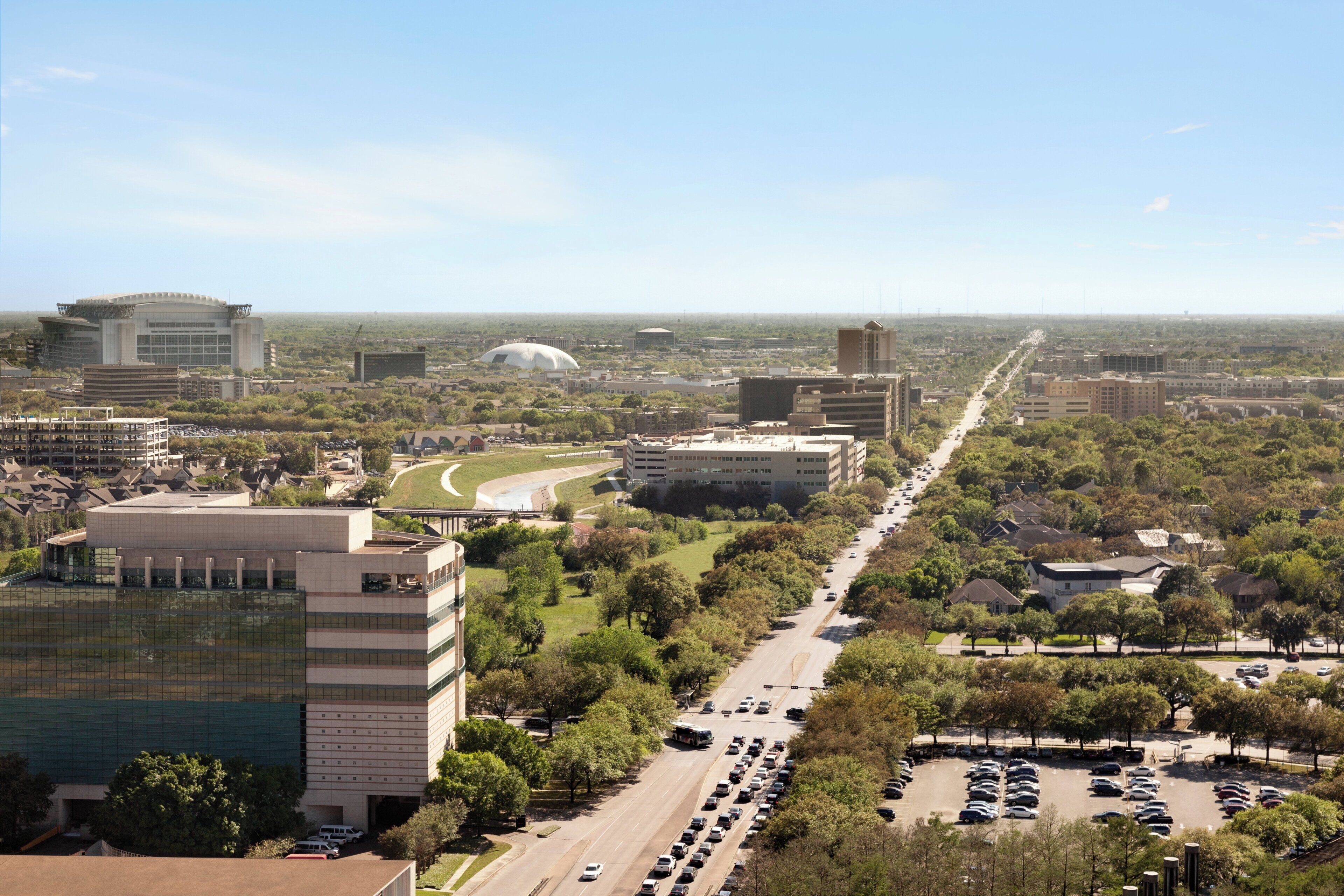 A cityscape with a prominent building with a curved roof, a large stadium, and a busy road with cars.