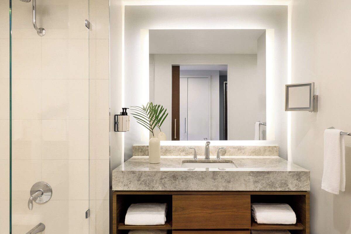 Une salle de bain moderne avec un grand miroir, un lavabo, une douche et des meubles de rangement en bois.