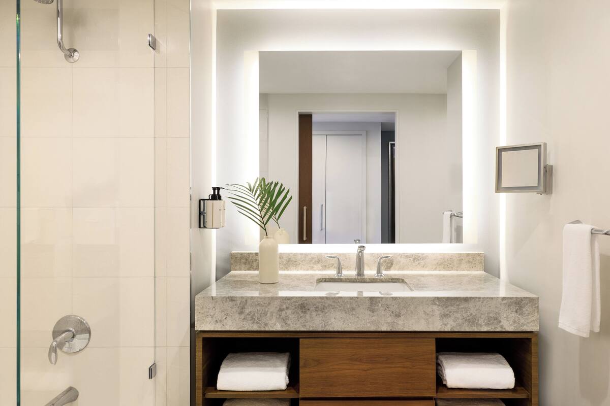 A modern bathroom with a large mirror, a sink, a shower, and wooden storage cabinets.