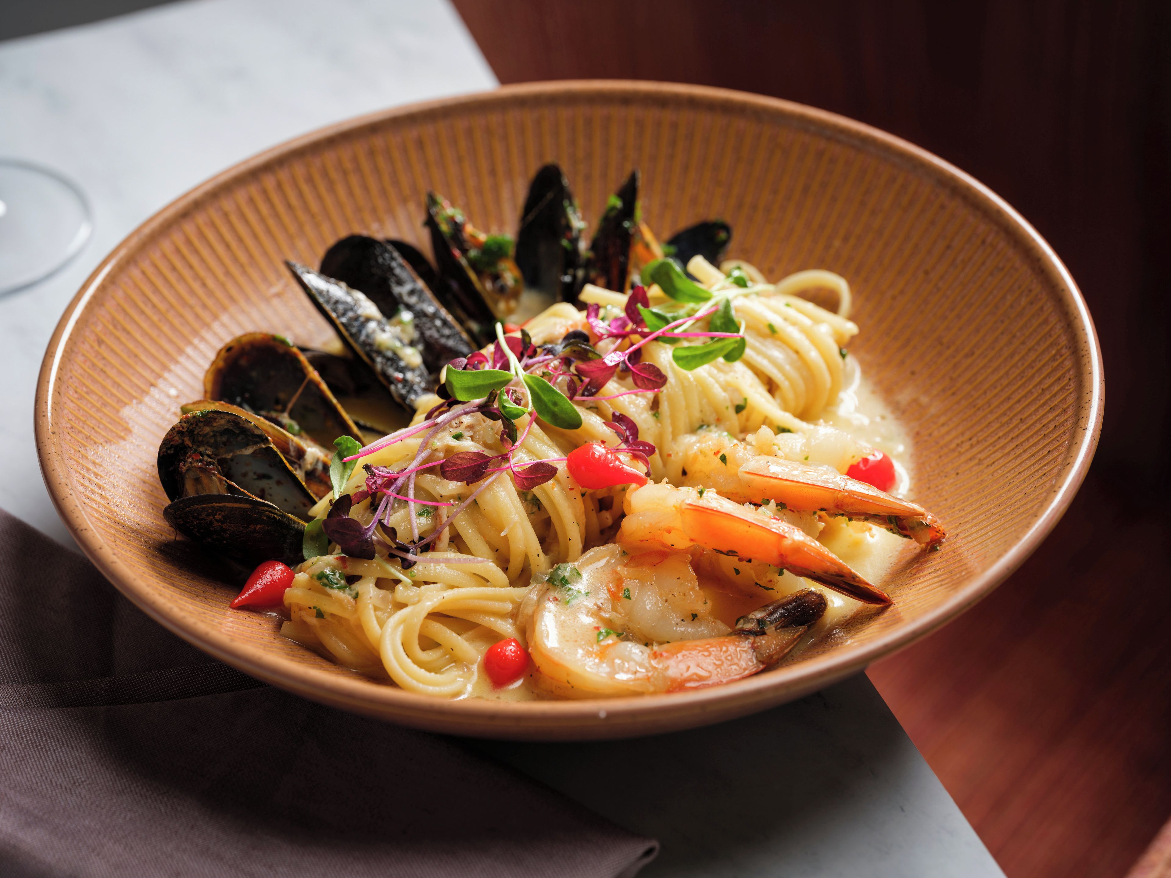 A bowl of pasta with seafood, garnished with herbs and vegetables.