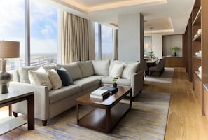 A modern hotel room with a sectional sofa, a coffee table, and a view of the city.