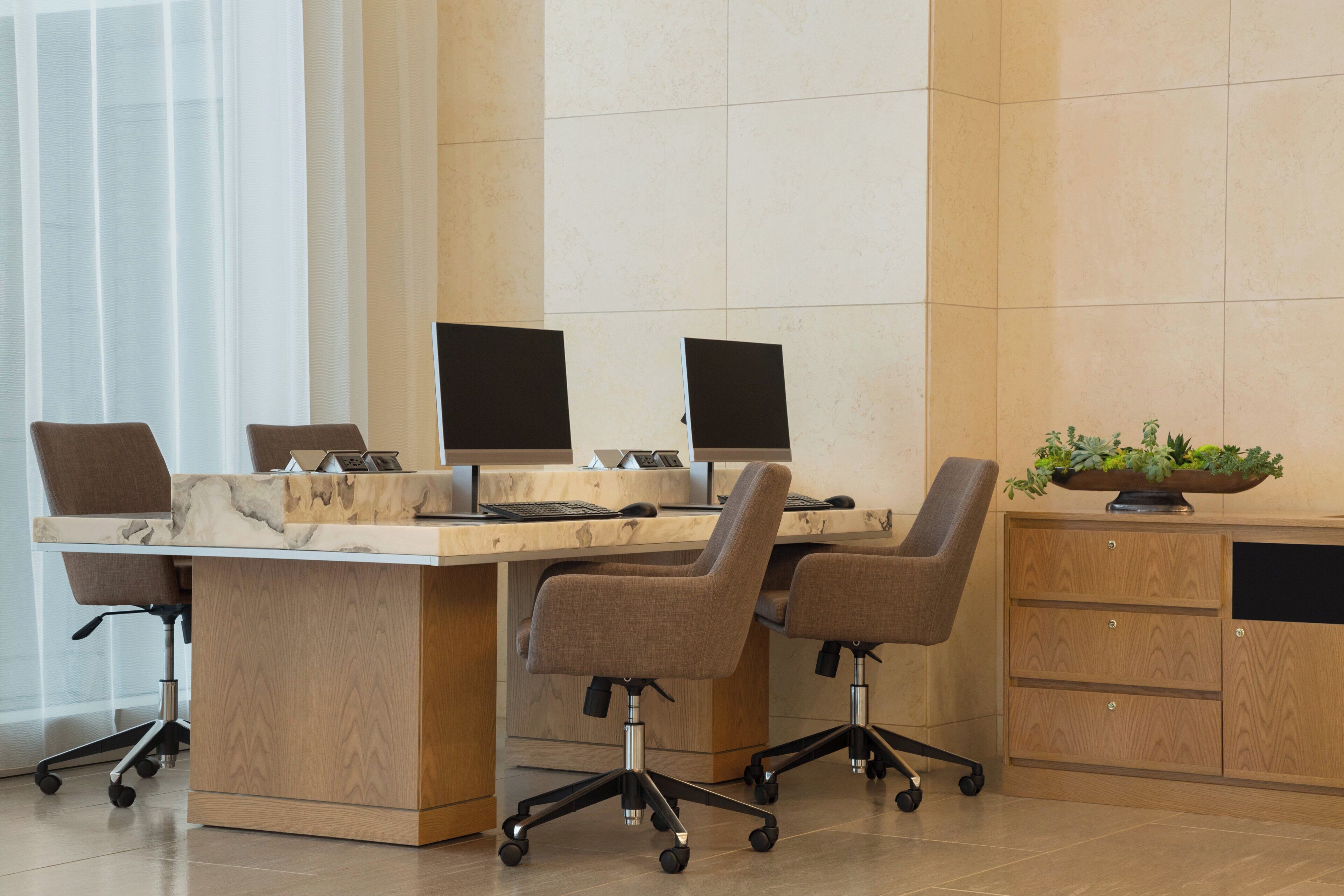 A modern office space with a marble desk, ergonomic chairs, and a wooden cabinet.